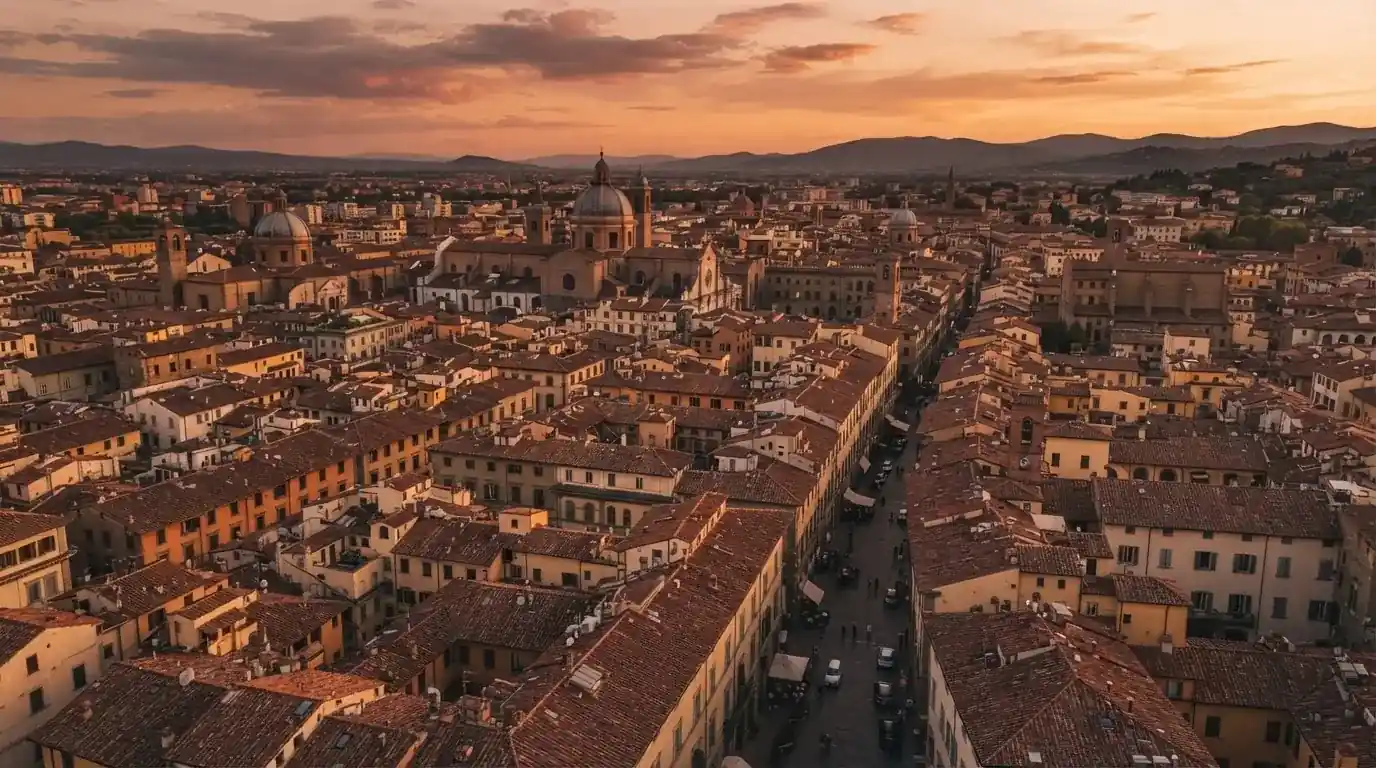 Vista dall'alto di una città italiana al tramonto con tetti in terracotta e cielo arancione.